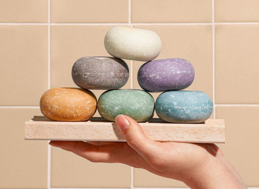 a hand holding a soap dish with shampoo bars stacked in a pyramid