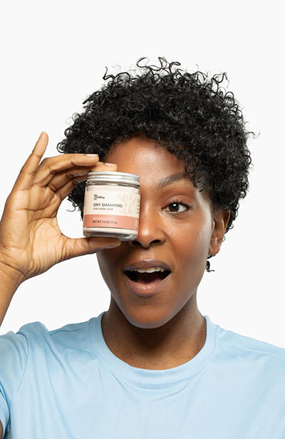 a woman holding a jar of dry shampoo in front of her eye