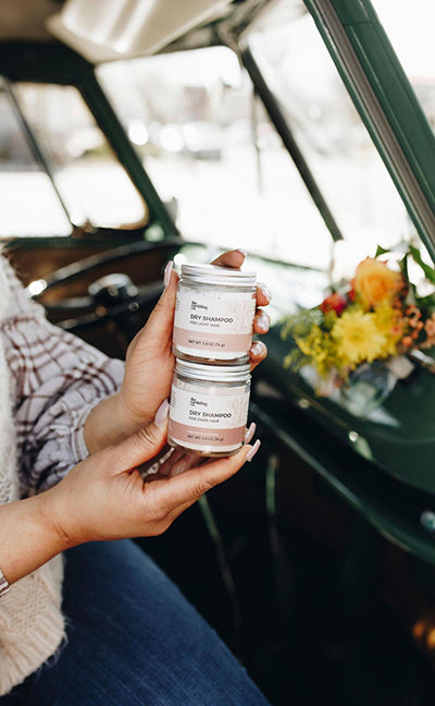 a woman holding two jars of dry shampoo