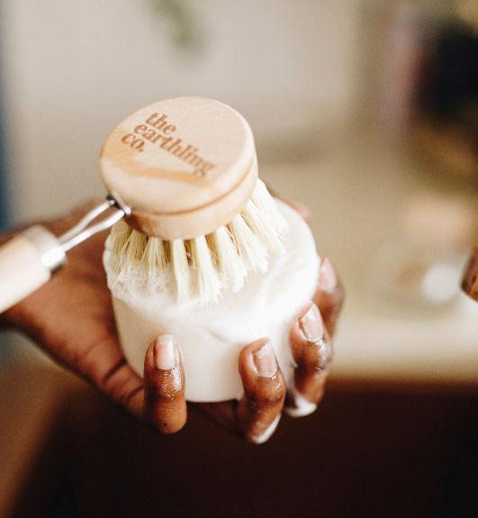 A person lathering up a scrub brush with solid dish soap