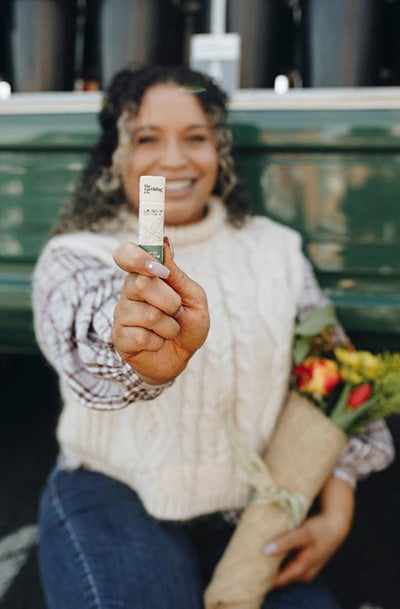 a smiling woman holding out a tube of earthling co peppermint lip balm